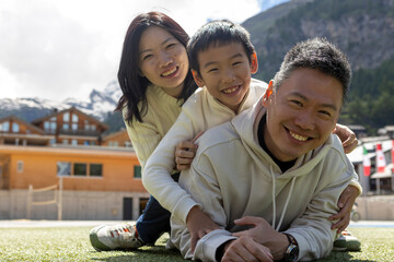 Happy family lying on grass in mountain resort: father, mother, and son smiling together