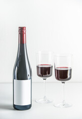 Red wine setting with bottle and two wine glasses on table at white background. Front view with copy space.