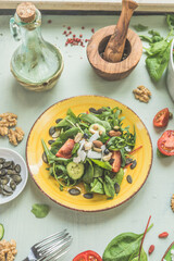 Healthy green vegan salad with nuts on yellow plate. Vegan salad topping and ingredients. Top view. Vegetarian lunch