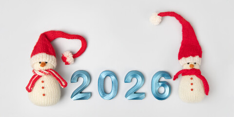 Knitted toy snowman in red hat and scarf with blue numbers 2026 on gray background. New Year's concept, greeting card, top view