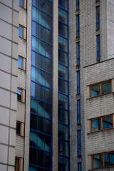 Close-up view of a modern office building with beige tiled facade and large blue-tinted glass windows. Reflections create dynamic patterns, emphasizing the vertical structure and urban architectural d