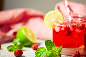 Glass of red raspberry drink with striped straw, lime and mint - fresh and playful summer vibe.