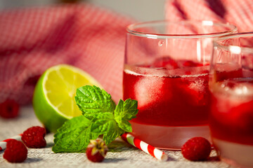 Fresh red drink with striped straw and green citrus on textured background. Natural light and vibrant freshness.