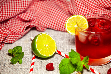 Fresh red drink with striped straw and green citrus on textured background. Natural light and vibrant freshness.
