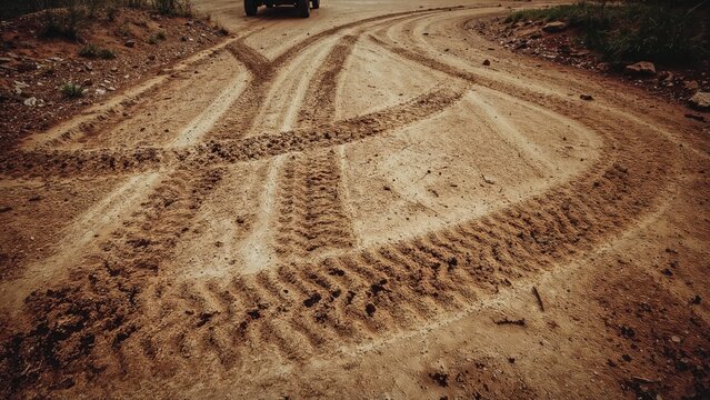 Tracks left by a car on earthy, sandy, or muddy ground, with a classic worn effect.