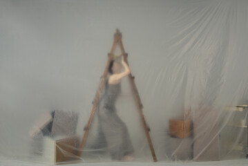 A woman climbing a ladder behind a translucent curtain.