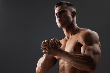 Muscular model sports young man on dark background. Fashion portrait of strong brutal guy. Male flexing his muscles.