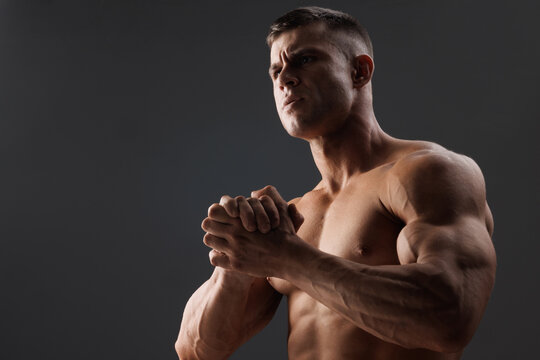 Muscular model sports young man on dark background. Fashion portrait of strong brutal guy. Male flexing his muscles.