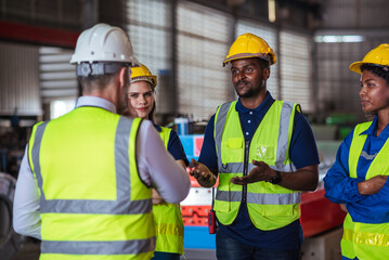 Diverse team of industrial workers wearing safety helmets and reflective vests receiving instructions from supervisor in manufacturing factory, focusing on teamwork, safety, and productivity.