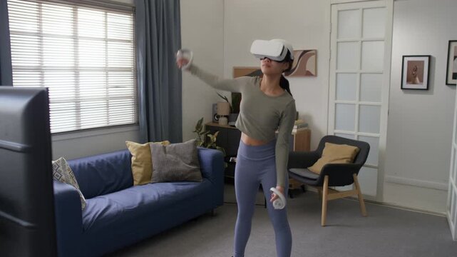 Teenage girl wearing virtual reality headset, cropped shirt and tights doing side bends during interactive workout at home