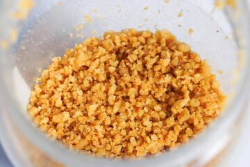 Close up crispy flakes kremesan topping in plastic jar isolated on horizontal background.