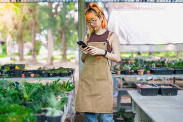 Asian Woman Business Owner Using Phone for Online Sales at Her Eco-Friendly Cactus Shop Market.
