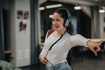 A cheerful young woman wearing headphones is energetically enjoying music in a modern indoor space. She appears joyful, fully immersed in the moment, creating a lively and vibrant atmosphere.