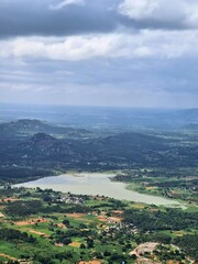 Fototapeta premium Expansive aerial view of a serene freshwater lake encircled by lush agricultural fields and small rural settlements, with distant hills fading into the horizon beneath a dramatic cloudy sky.