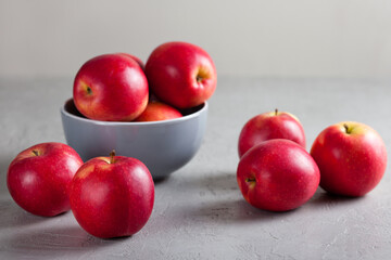 A gray ceramic bowl filled with red apples sits on a textured gray surface. Soft natural light create a calm, minimalist food scene. The concept of proper healthy nutrition 