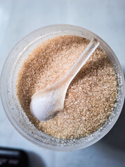 Close-up top view of white granulated sugar in a transparent container with a plastic spoon, perfect for food photography, sweetener concept, kitchen ingredient, baking, and culinary background.