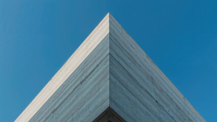 Side view of a minimalist building exterior with abstract triangular concrete wall elements set against a vibrant blue sky