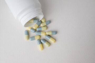 Top view white bottle container with medication capsules on light grey background with copy space.