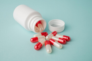 Close up bottle container with red and white medication capsules on blue background with copy space.