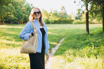 Young 30s blonde woman with bag smiling at the park. Lifestyle, fashion, people concept.