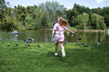 A running girl chases away pigeons in a park on a summer day.