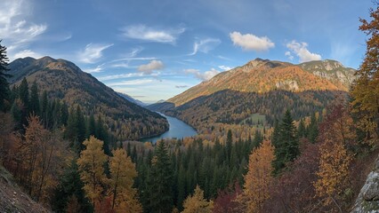 Obraz premium Broad perspective of a beautiful valley with a river bordered by forested slopes and rugged mountains