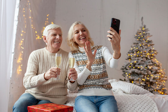 elderly couple of seniors in sweaters celebrate the New Year at home drinking champagne and taking selfies on smartphone, grandfather and grandmother communicate via video call on Christmas - Powered by Adobe