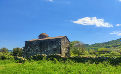 Obraz premium Historic stone church with domed roof. Stone building topped with a domed roof sits behind a low stone wall in a lush green field under a bright blue sky. perfect for travel and architecture.