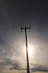 Obraz premium A tall power pole is silhouetted against a cloudy sky