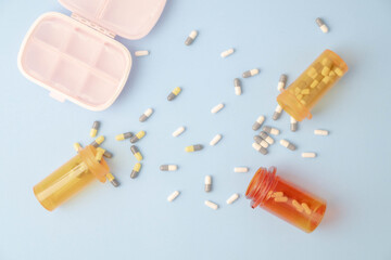 Multiple medication capsules spilling out of bottles onto blue background with a pink meds organizer.