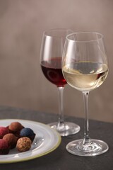 Delicious truffle bonbons and wine on black table against grey background