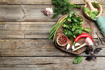 Different fresh herbs, spices, scissors, thread, mortar and pestle on wooden table, flat lay. Space for text