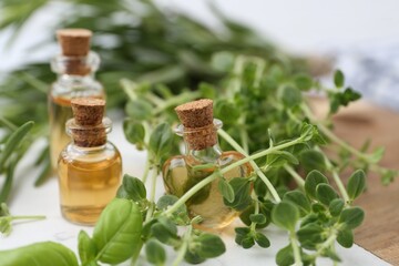 Bottles of essential oil and herbs on white marble table, closeup