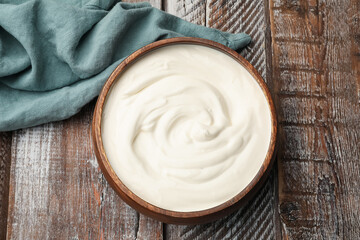 Delicious sour cream in bowl on wooden table, top view