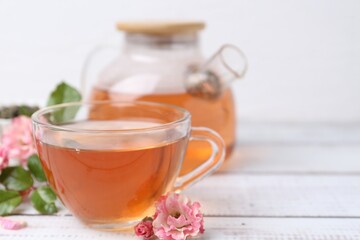 Tasty rose tea and flowers on white wooden table, closeup. Space for text