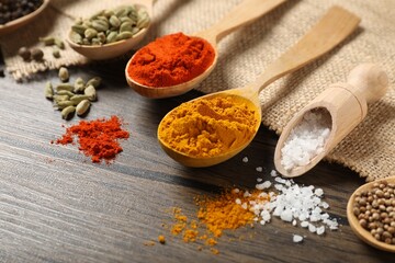 Different aromatic spices in spoons and scoop on wooden table, closeup