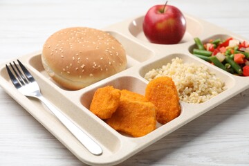 Plastic tray with tasty food and fork on light wooden table, closeup. School lunch