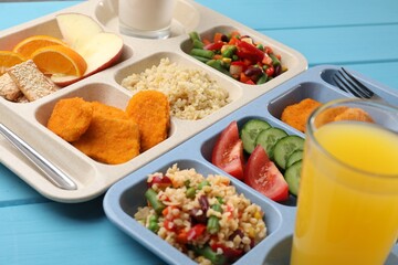 Plastic trays with tasty food, orange juice and milk on light blue wooden table, closeup. School lunch