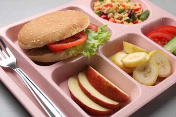 Plastic tray with tasty food and fork on grey table, closeup. School lunch