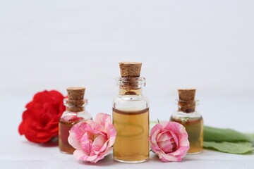 Bottles of cosmetic products, roses and sage on white table, closeup