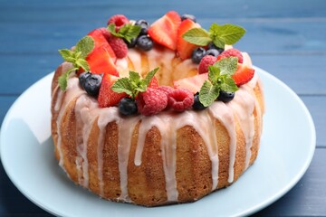 Delicious bundt cake with berries, glaze and mint on blue wooden table, closeup