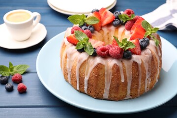 Delicious bundt cake with berries, glaze and mint on blue wooden table, closeup
