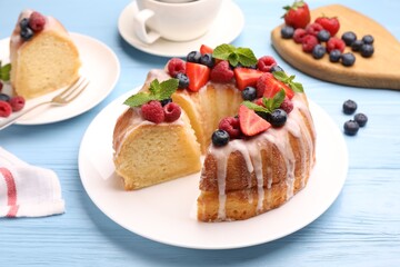 Pieces of delicious bundt cake with berries, glaze and mint on light blue wooden table, closeup