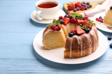 Pieces of delicious bundt cake with berries, glaze and mint on light blue wooden table, closeup
