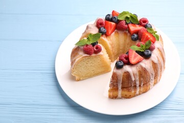 Pieces of delicious bundt cake with berries, glaze and mint on light blue wooden table, closeup