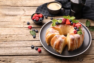 Pieces of delicious bundt cake with berries, glaze and mint on wooden table, closeup