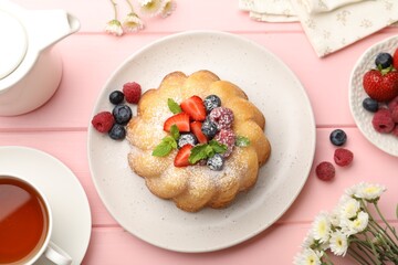 Delicious bundt cake with powdered sugar, berries and mint on pink wooden table, flat lay