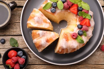 Pieces of delicious bundt cake with berries, glaze and mint on wooden table, flat lay