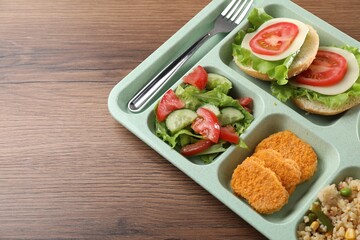 Plastic tray with tasty food and fork on wooden table, closeup. School lunch