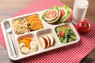 Plastic tray with tasty food, milk and fork on wooden table, closeup. School lunch
